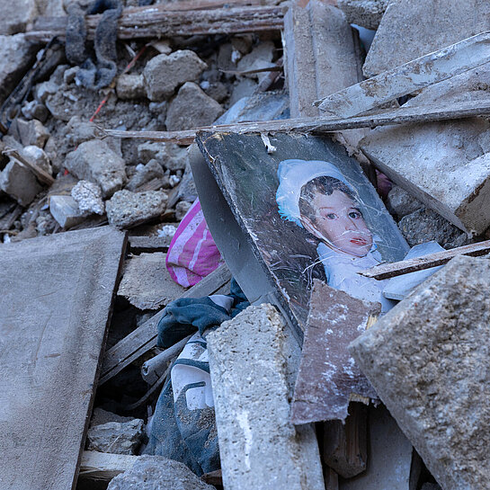 Trümmerteile von Häusern liegen auf dem Boden, darin liegt ein Bild von einem Kind