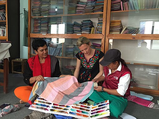 Plan Shop-Geschäftsführerin Dorothee Ingwersen besuchte vor der Corona-Pandemie die Maheela-Kooperative in Nepal. Gemeinsam wählten sie Farb- und Stoffmuster aus. Frauen suchen Farbmuster auf dem Boden aus.