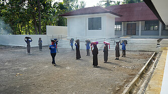 Kinder stehen auf einem Schulhof und halten sich ihre Rucksäcke über den Kopf