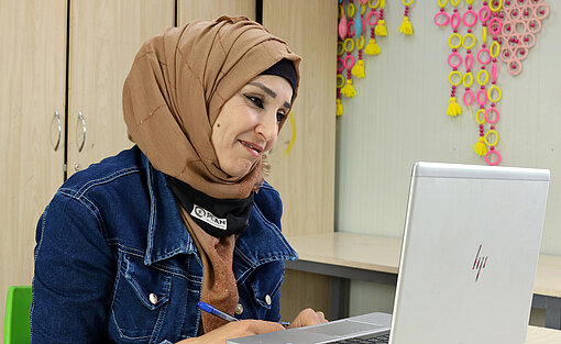 Plan International bietet in Azraq eine Vielzahl von Programmen an. Vor allem sollen Frauen und Mädchen angesprochen werden. Alia sitzt arbeitend vor einem Notebook.