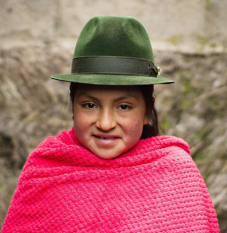 Ein Mädchen mit Hut und pinkem Poncho schaut in die Kamera