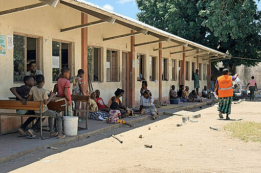 Blick auf ein flaches Gebäude, vor dem Mneschen auf Kisten hocken
