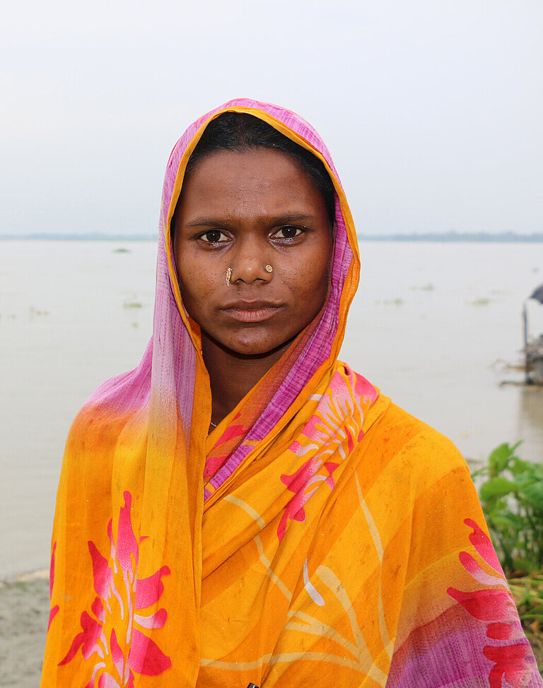 eine Frau steht an einem Ufer, hinter ihr sieht man Wasser