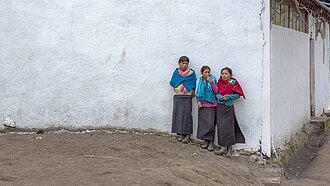 Drei Schulmädchen stehen an der Wand vor ihre Schule in den Anden.