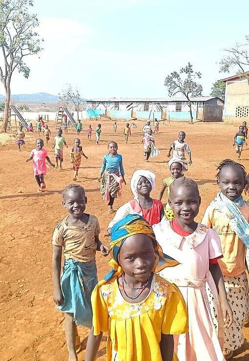 In den Geflüchtetenlagern leben die Kinder zum Teil ohne ihre Eltern, weil die im Kriegsgebiet zurückbleiben Eine Gruppe Kinder spielt ausgelassen und läuft auf einem sandigen Platz Richtung Kamera