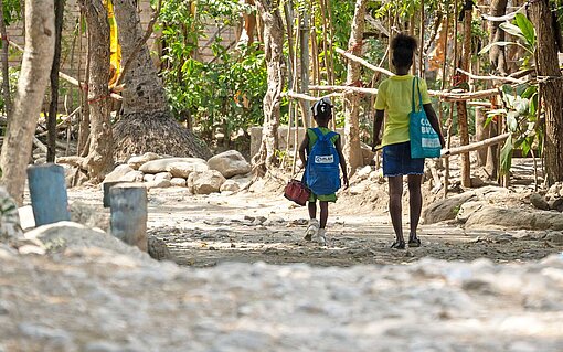 Humanitäre Hilfe von Plan International Haiti erreicht Familien in abgelegenen Regionen Mutter und Tochter laufen in einem Dorf