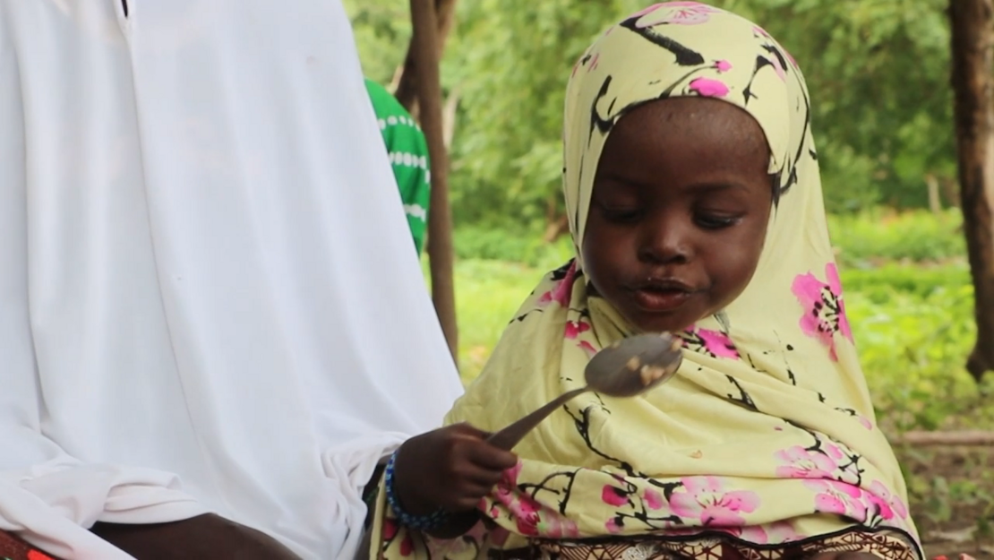 Thumbnail Video: Ein kleines Mädchen hält einen vergleichsweise sehr großen Löffel mit Reis in der Hand.