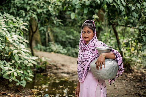 Aysha (18) ist im Distrikt Bhola in Bangladesch gerade dabei, Wasser zu holen Mädchen im Wald mit Wasserkrug unter dem linken Arm