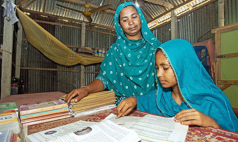 Zwei Frauen mit grünen Kopftüchern beugen sich über einen Tisch mit Büchern und Schreibmaterial