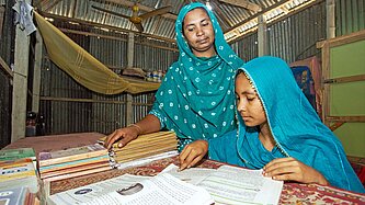 Zwei Frauen mit grünen Kopftüchern beugen sich über einen Tisch mit Büchern und Schreibmaterial