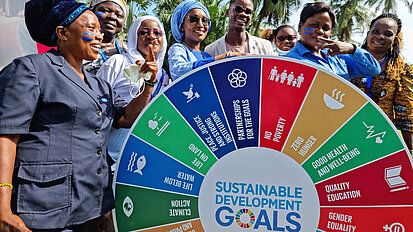Bild: Eine Gruppe junger Erwachsene mit einer Drehscheibe, auf der die Sustainable Development Goals abgebildet sind
