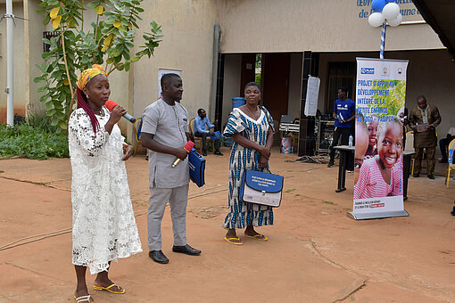 Junge Frau in weißem Kleid mit Mikrofon neben zwei anderen Vortragenden