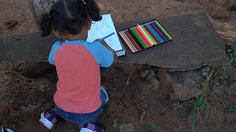 Ein vierjähriges Mädchen mit Zöpfen von hinten, es malt etwas in ein Malbuch