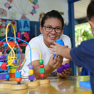 Eine Frau reicht einen blauen Bauklotz an ein junges Mädchen.
