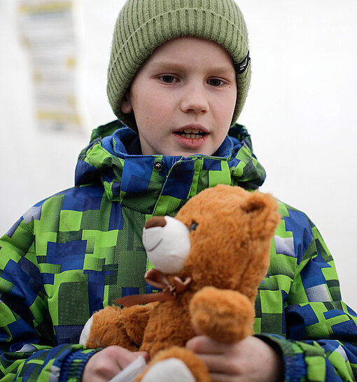 Ein junge mit Wintermütze und Jacke hält einen Plüschteddy in der Hand