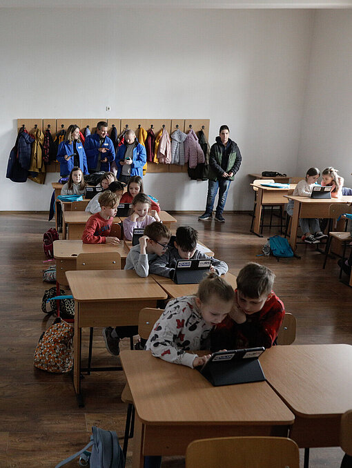 Geflüchtete Kinder in einem temporären Lernraum Kinder sitzen in einem Klassenzimmer und schauen jeweils zu zweit auf einen Tablet-Computer