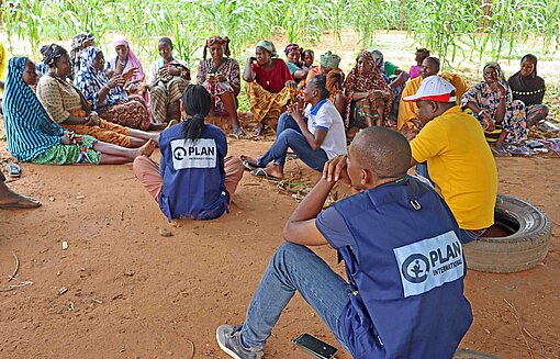Plan-Teams beraten Gemeindemitglieder in Burkina Faso zu Ernährungsfragen Leute sitzen auf einem Dorfplatz
