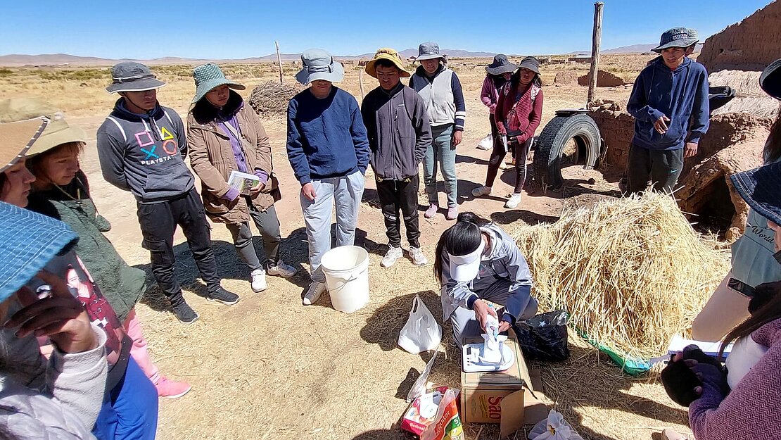 Eine Gruppe Jugendlicher hat sich im Kreis versammelt und schaut dem Lehrer zu