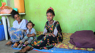 Mutter mit zwei Töchtern sitzt auf Matratze in einfachem Raum mit grün gestrichener Wand in Äthiopien