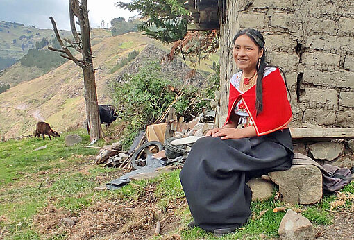 Ein Mädchen sitzt vor einer Hütte in den Anden