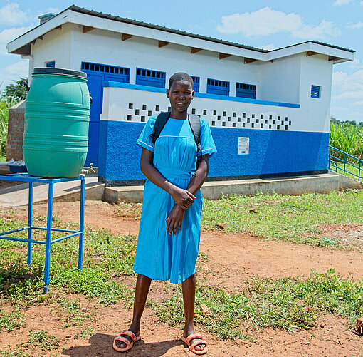 Shadia vor dem neu gebauten Toilettenblock an ihrer Schule Ein Mädchen im blauen Kleid steht lächelnd vor dem neu gebauten Toilettenblock an ihrer Schule