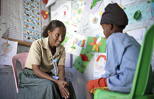 Eine Frau beugt sich zu einem Jungen herunter und hört ihm zu
