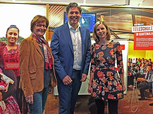 Zwei Frauen und ein Mann stehen aufgereiht zum Foto vor einer Ausstellungswand