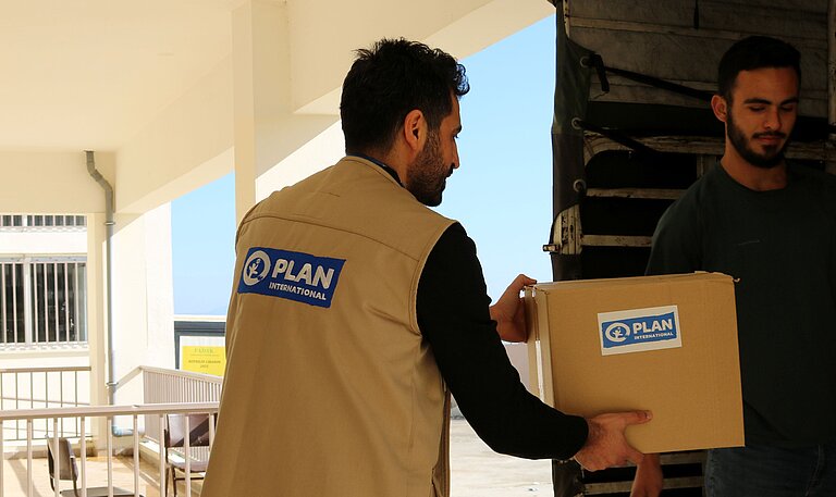Plan Mitarbeiter bringt ein Paket mit Schulutensilien in den Südlibanon