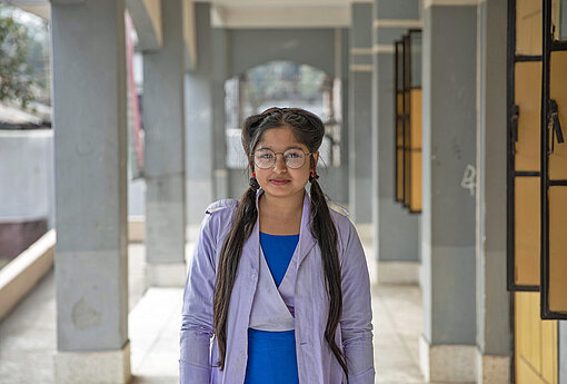 Akhimoni (15) aus dem Norden von Bangladesch berichtet in der Plan Post über Herausforderungen in ihren Alltag Eine junge Frau steht vor ihrer Oberschule