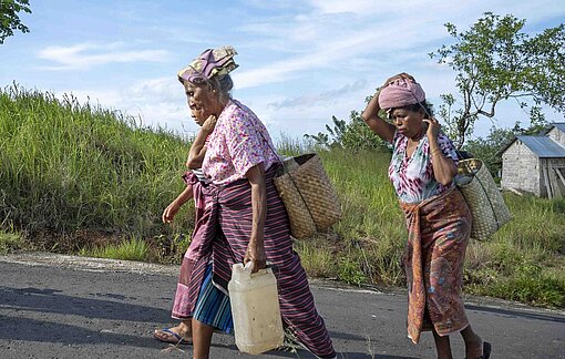Frauen aus Nagekeo tragen Kanistern voll Wasser zurück in ihr Dorf  Drei Frauen in bunten Kleider tragen schwere Kanister mit Wasser