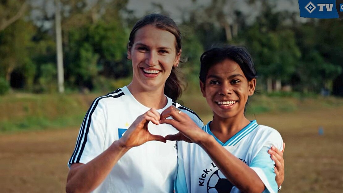 Eine junge Frau mit weißem HSV-Trikot steht zusammen mit einem dunkelhaarigen kleinen Mädchen in dunkelblauem HSV-Trikot zusammen.