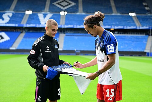 Zwei HSV-Spieler stehen sich im Stadion gegenüber und unterzeichnen ein HSV-Trikot