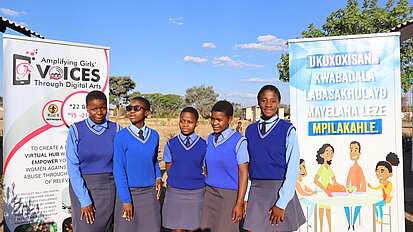 Junge Frauen stehen vor Plakaten zur Stärkung von Mädchen