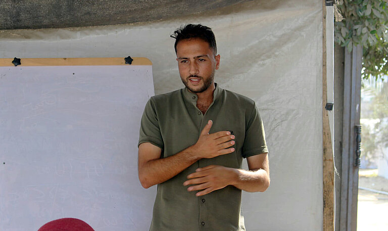 Mohammed steht vor einem Flipboard und spricht zu einer Gruppe Menschen