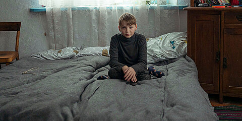 Ein Junge sitzt auf einem Bett mit warmen Decken