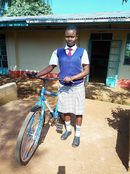 Magdaline steht neben einem blauen Fahrrad. 