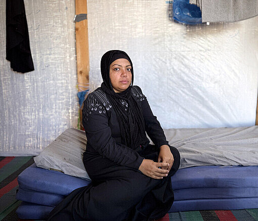 Mutter aus Gaza sitzt in schwarz gekleidet in einem Zelt auf einer Matratze