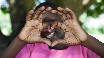 Ein Mädchen aus Uganda formt mit ihren Händen ein Herz und lächelt in die Kamera