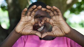 Sinnvolle Geschenke Ein Mädchen aus Uganda formt mit ihren Händen ein Herz und lächelt in die Kamera