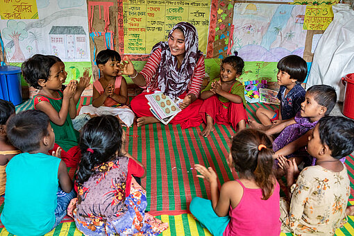 Nach einem Workshop von Plan International achtet Jamila bei ihrer Kindergartenlasse auf die Gleichberechtigung der Geschlechter. Kleine Kinder sitzen mit einer Lehrerin im Kreis auf dem Boden.