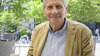 Ulrich Wickert sitzt mit einem Glas Wasser an einem Tisch im Freien.