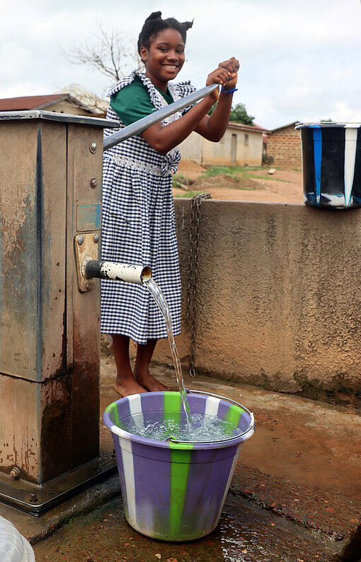 Die zwölfjährige Marie-Rose steht mit einem Eimer Wasser am neuen Brunnen auf dem Gelände ihrer Schule in Guinea.