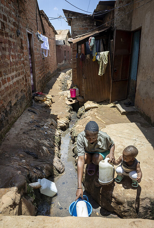 Faith mit ihrer Tochter kniend holen Wasser aus einem Bach 