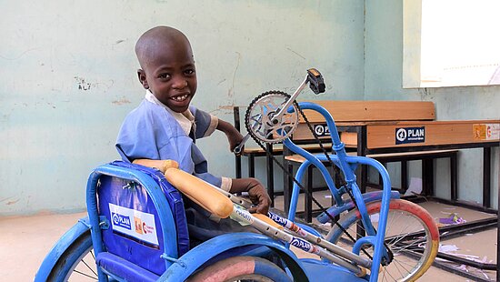 Bild: Ein kleiner Junge im Schulraum, er sitzt auf einem Rollstuhl
