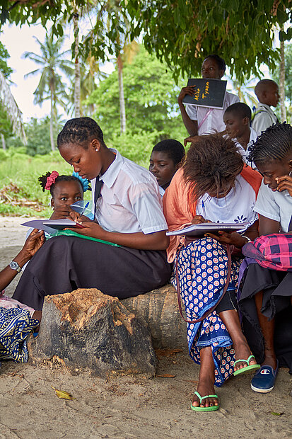 Schüler:innen sitzen auf einem Stein und schreiben
