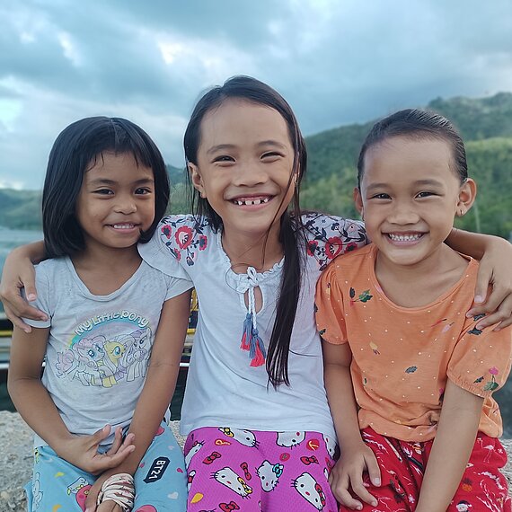 Ein Mädchen legt die Arme um die Schulter ihrer Freundinnen und lächelt