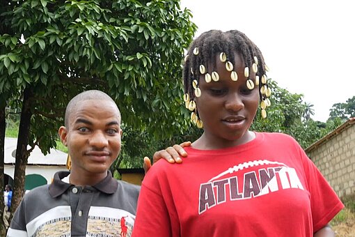 Ein junger Mann hat die Hand auf die Schulter einer jungen Frau gelegt, sie laufen gemeinsam zur Schule