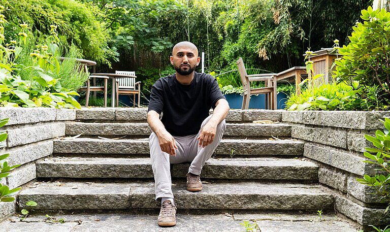 Ein Mann sitzt in inem Garten auf einer Treppe.