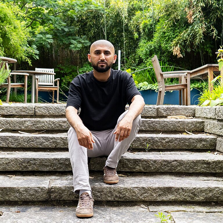 Ein Mann sitzt in inem Garten auf einer Treppe.