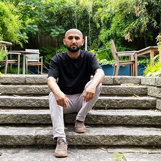 Ein Mann sitzt in inem Garten auf einer Treppe.